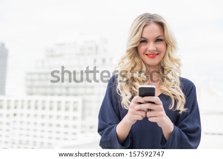 Cheerful gorgeous blonde with red lips texting on urban background