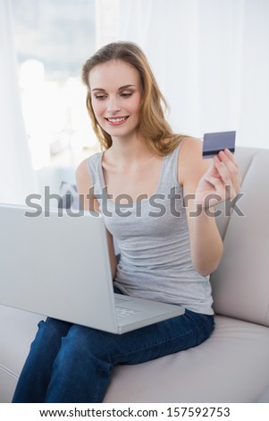 Pretty woman sitting on couch using laptop for online shopping at home in the living room