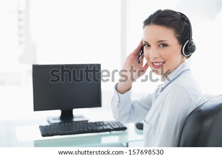 Smiling stylish brunette operator answering a call in bright office