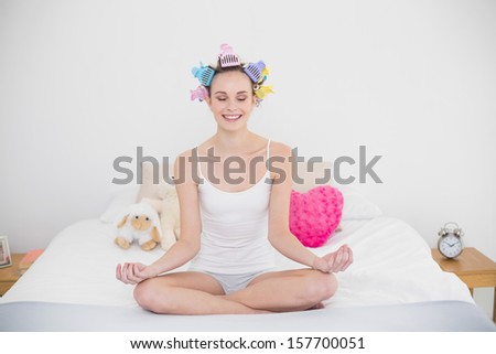 Peaceful natural brown haired woman in hair curlers practicing yoga in bright bedroom