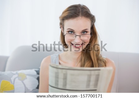 Happy young woman sitting on sofa holding newspaper at home in the sitting room