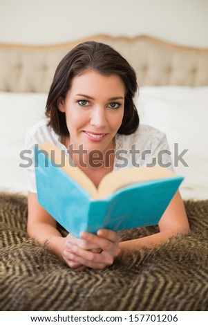 Smiling pretty brown haired woman reading a book in a chic bedroom