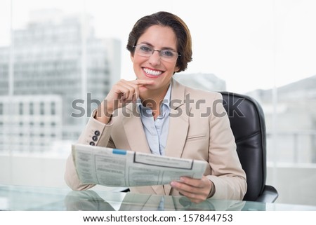 Businesswoman holding newspaper at her desk in bright office