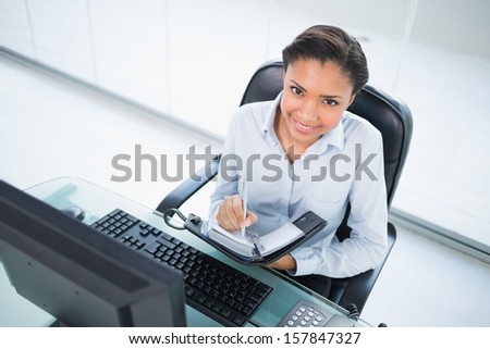 Happy young dark haired businesswoman taking notes on her schedule in bright office