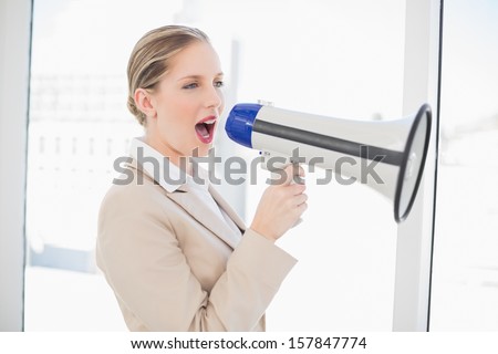 Energetic blonde businesswoman in bright office shouting in megaphone