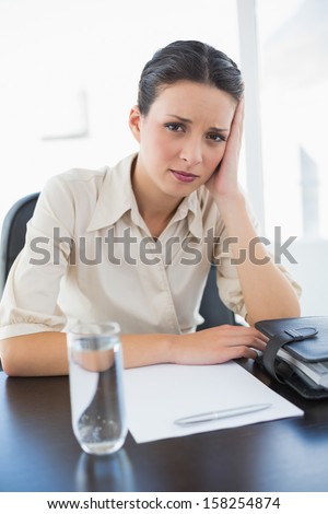 Frowning stylish brunette businesswoman sitting and holding her head in bright office