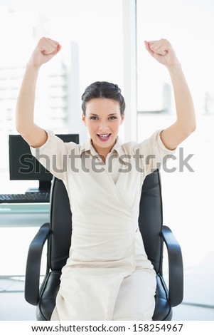 Cheering stylish brunette businesswoman raising her arms in bright office