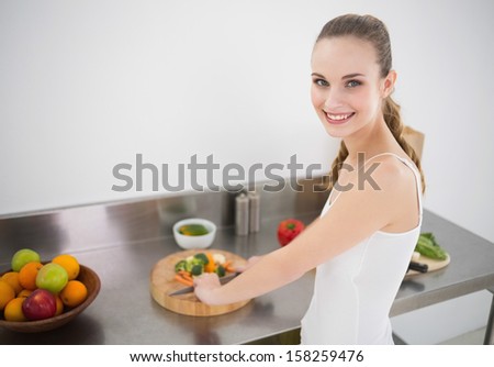 Pretty young woman preparing vegetables smiling at camera in the kitchen at home