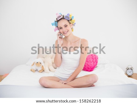 Delighted natural brown haired woman in hair curlers making a phone call in bright bedroom
