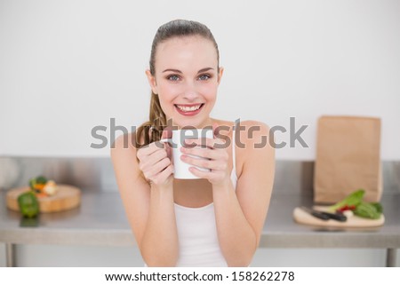 Happy young woman holding mug in the kitchen at home