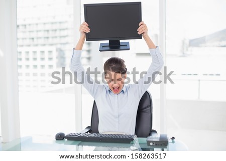 Angry classy brown haired businesswoman throwing her computer screen in bright office