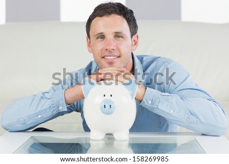 Cheerful casual man resting head on piggy bank in bright living room