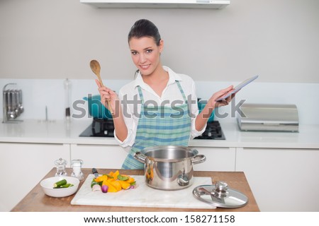Smiling gorgeous woman wearing apron using tablet while cooking in bright kitchen