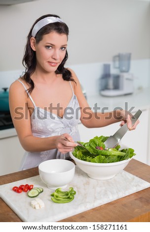 Smiling cute brunette mixing healthy salad in bright kitchen