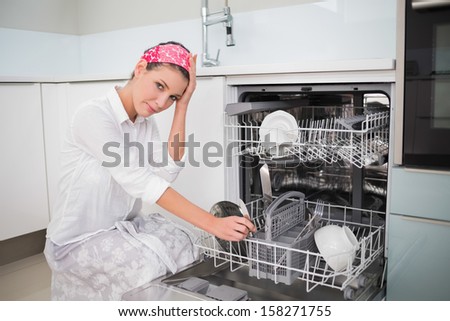 Worried charming woman using dish washer in bright kitchen