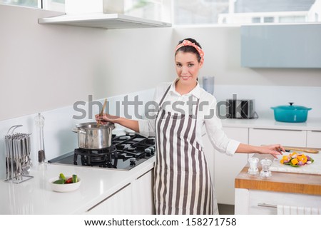 Cheerful pretty woman with apron cooking in bright kitchen