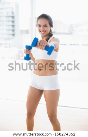 Smiling sporty woman using dumbbells in bright room