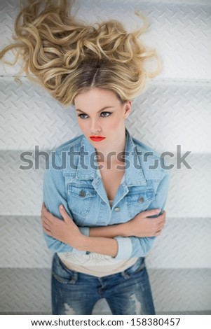 Thinking blonde wearing denim clothes lying on stairs looking away