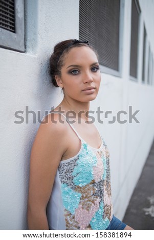 Attractive woman leaning against a white wall and looking at camera