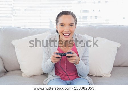 Smiling woman sitting on sofa in bright living room playing video games