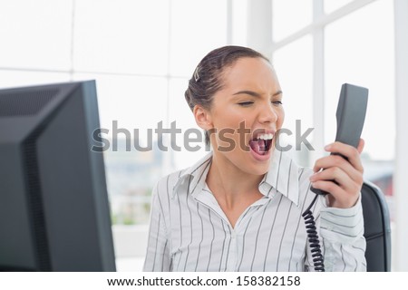 Angry businesswoman screaming at phone in her office