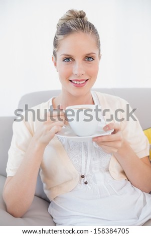 Smiling fresh model holding coffee sitting on sofa in bright living room
