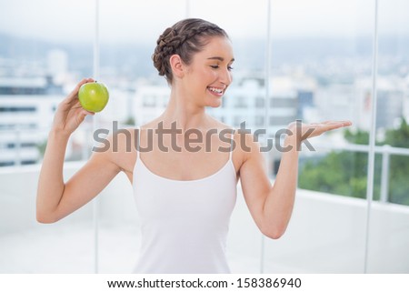 Happy sporty brunette holding green apple in bright fitness studio