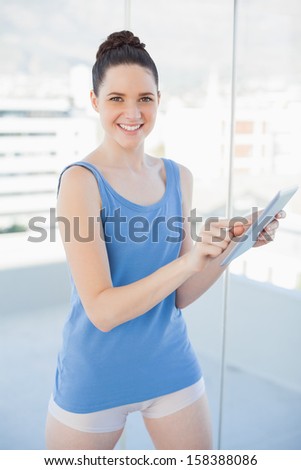 Smiling gorgeous woman in sportswear using tablet pc in bright sports hall