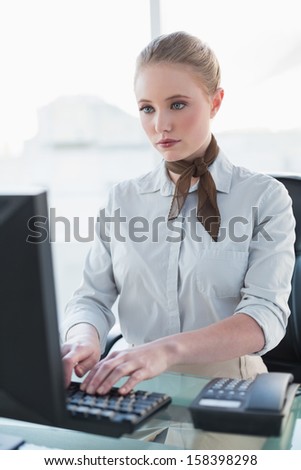Blonde stern businesswoman working on computer in bright office
