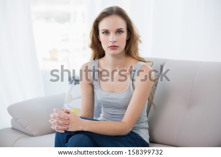 Stern young woman sitting on couch at home in the living room