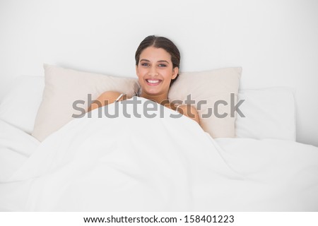Peaceful young brown haired model in white pajamas lying in her bed in bright bedroom