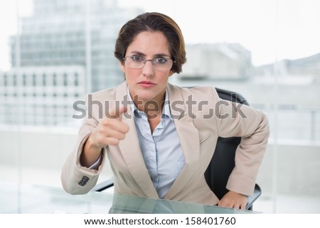Angry businesswoman pointing at camera in bright office