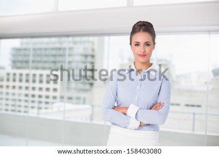 Content brunette businesswoman standing with arms crossed in bright office