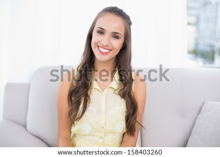 Cheerful pretty brunette sitting on coach in bright living room