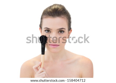 Serious natural brown haired model holding a blush brush on white background