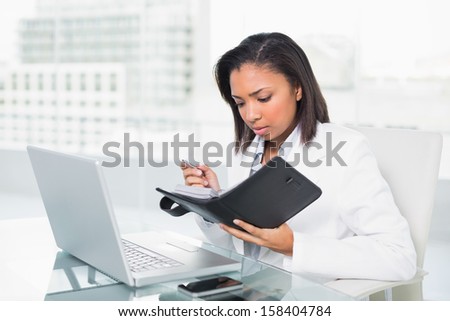 Anxious young dark haired businesswoman filling her schedule in bright office