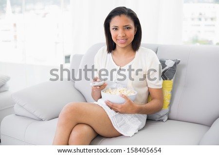 Calm young dark haired woman in white clothes watching television in a living room