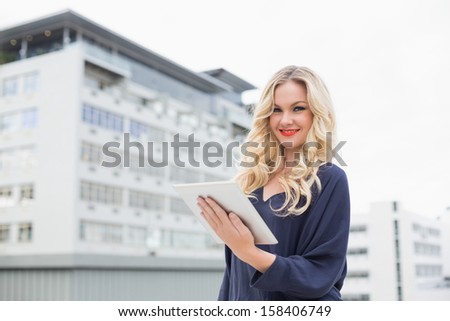 Smiling gorgeous blonde with red lips holding tablet on urban background