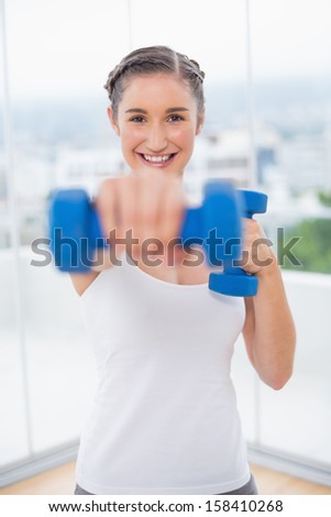 Happy athletic brunette exercising with dumbbells in bright fitness studio