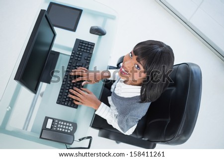 Overhead of smiling pretty businesswoman in bright office typing