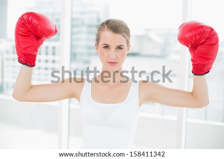 Competitive fit woman with red boxing gloves cheering up in bright sports hall