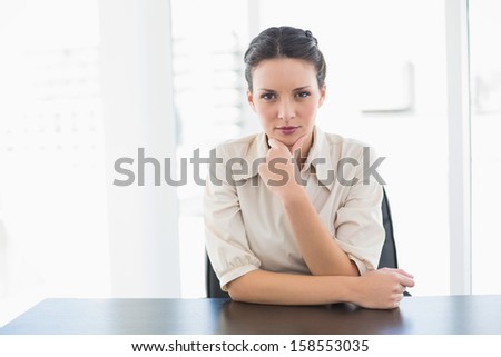 Frowning stylish brunette businesswoman looking at camera and holding her head in bright office