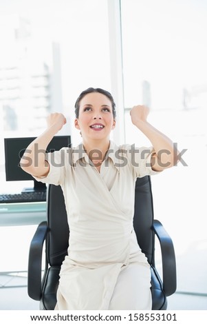 Happy stylish brunette businesswoman raising her fists in bright office