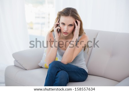 Stressed young woman sitting on couch talking on smartphone at home in the living room