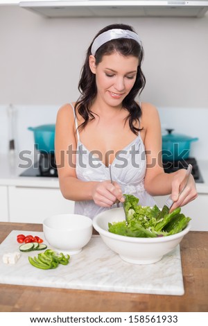 Happy pretty brunette mixing healthy salad in bright kitchen
