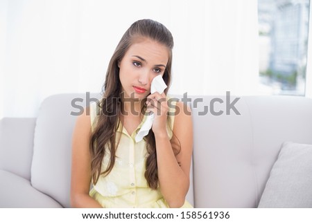 Sad attractive brunette holding a tissue in bright living room