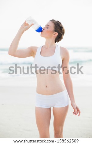 Peaceful slim brown haired model in white sportswear drinking water on the beach