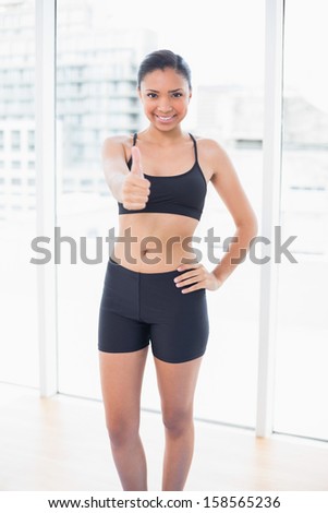 Content dark haired model in sportswear giving a thumb up in bright fitness studio