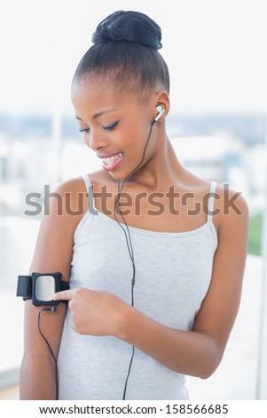 Smiling woman in sportswear listening to music and using her music player in bright room at home