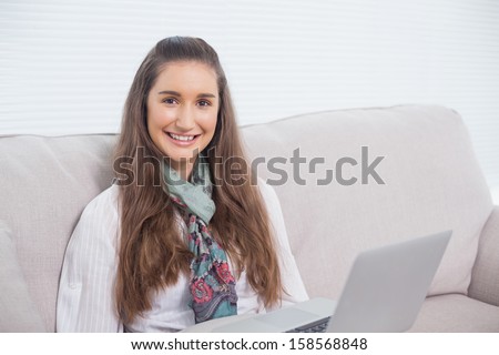 Happy gorgeous model using laptop sitting on sofa in bright living room